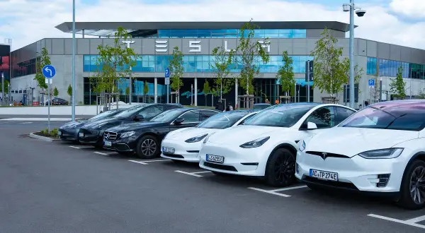 Rząd białych i czarnych Tesli zaparkowany przed budynkiem z napisem "TESLA". Czy to Tesla z jakiego kraju?