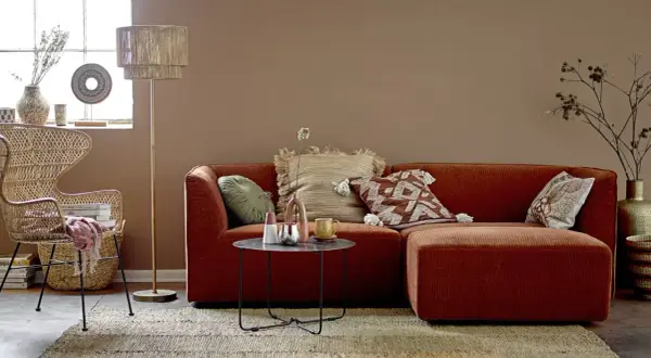 Przytulny salon w stylu boho. Pomarańczowa kanapa, wiklinowy fotel i dywan tworzą ciepłą paletę kolorów ziemi.