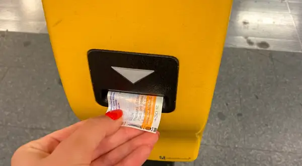 Dłoń z czerwonym lakierem wkłada do żółtego automatu bilet do praskiego metra. Bilet ma nadruk "30 Kč".