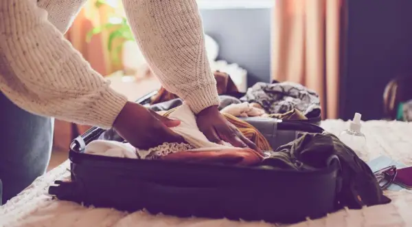 Person packt Kleidung in einen Koffer für den Urlaub. Die Packliste für den Urlaub ist fast komplett.