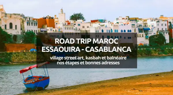 Bateau coloré sur la rive d'une ville côtière marocaine, avec des bâtiments blancs et bleus en arrière-plan.