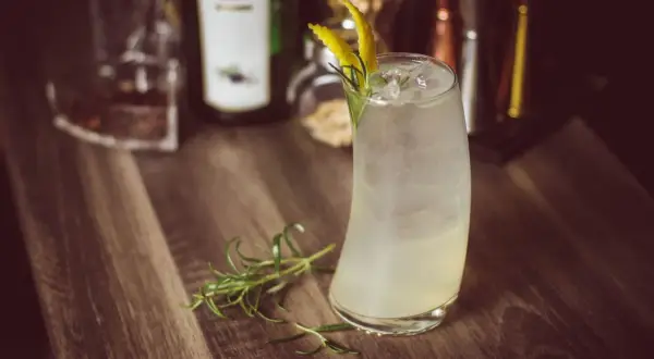 Orzeźwiający drink z lodem i cytrynową skórką, przypominający bombay sunset. Gałązka rozmarynu dodaje aromatu.