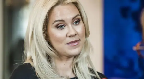 Caroline Hainer, med blont hår och makeup, ser åt sidan. En mikrofon syns i förgrunden.