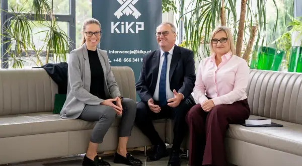 Trzy osoby siedzą na kanapie przed banerem z logo KiKP.