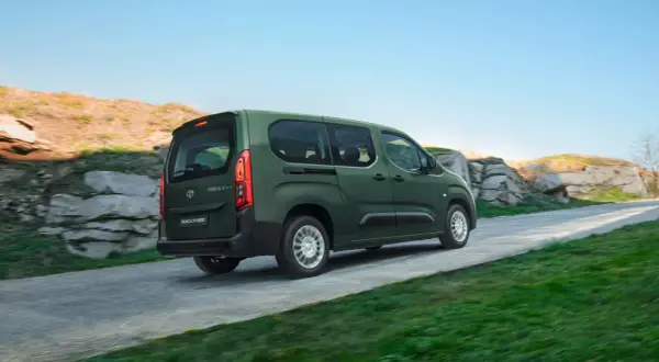 Zielony, używany Toyota Proace City Verso jedzie po krętej drodze wśród skał i zieleni.