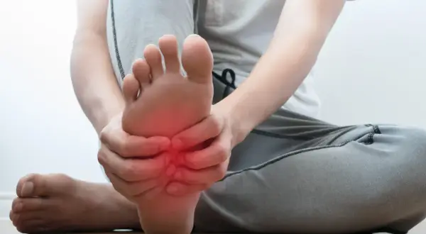 Persona che si tiene il piede, con un'area rossa che indica dolore sotto pianta del piede al centro.