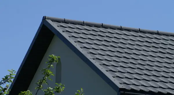 Szary dach z dachówki ceramicznej, idealny do obliczenia, ile dachówek na m2 roben. W tle błękitne niebo i fragment ściany domu.