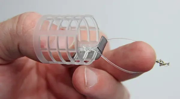 Ein Finger hält einen selbstgebauten Futterkorb mit Blei und Schnur.