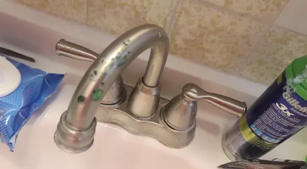Rubinetti del bagno con calcare verde incrostato. Accanto, salviettine e una bomboletta di schiuma da barba.