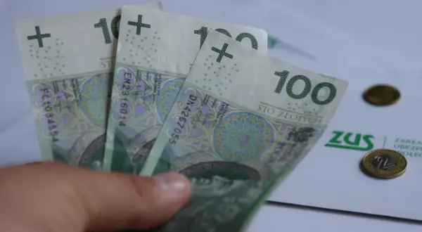 Dłoń trzyma banknoty 100 zł. Na papierze ZUS i monety. Czy to wystarczy na rentę na kręgosłup?