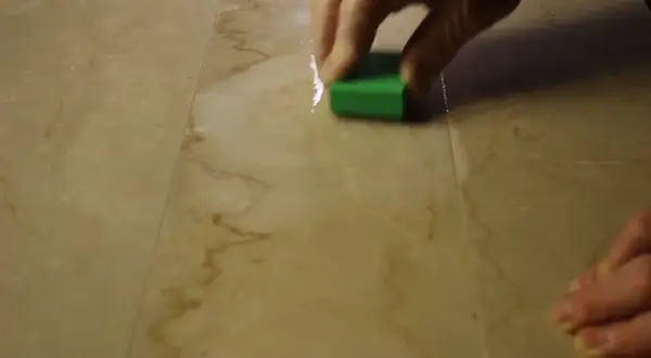 Mano che lucida un marmo corroso con una spugna verde.