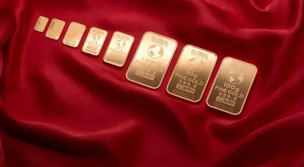 Sztabki złota Global Intergold, od najmniejszej do 100g, ułożone na czerwonym jedwabiu. Wśród nich widać combibar Valcambi.