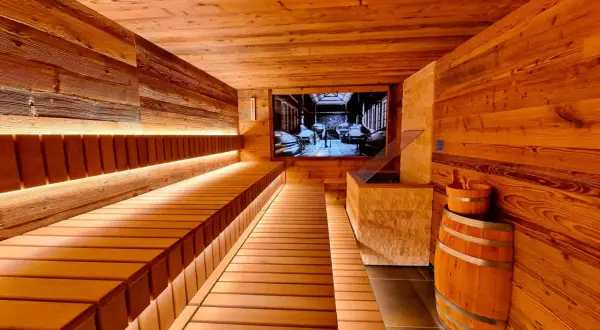Gemütliche Holzsauna mit beleuchteten Bänken und einem Bild von einer Brauerei an der Wand. Ein Bierfass und ein Holzeimer stehen bereit für ein entspannendes Bier-Spa-Erlebnis.