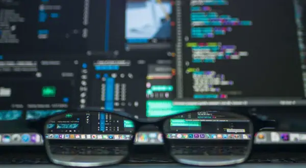 Okulary na tle ekranu z kodem. Programista analizuje kody PKD, tworząc nowe projekty.