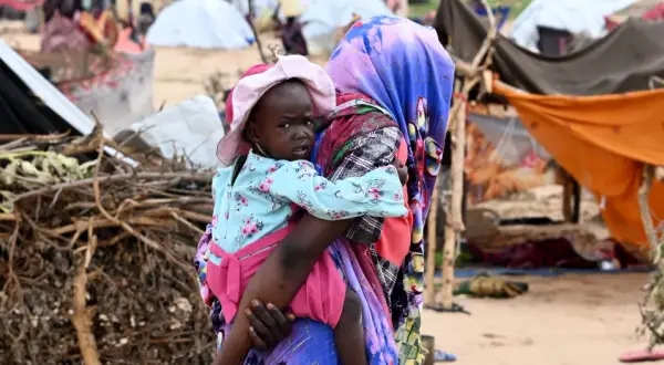 En kvinna bär ett barn i en flyktinglägerliknande miljö. Detta ger en inblick i fakta om Sudan och dess utmaningar.