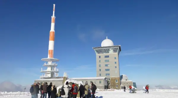 Menschen stehen im Schnee vor dem Brocken-Wetterturm und dem Fernsehturm. Ein sonniger Tag im Winter auf dem Brocken.