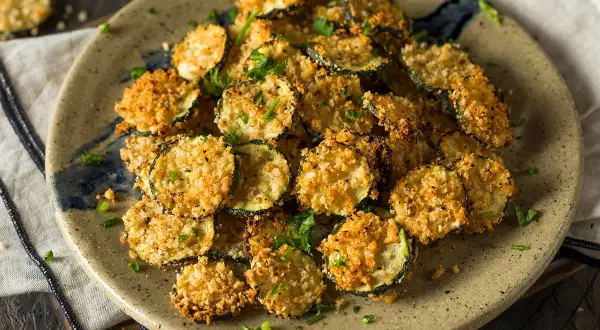Fette croccanti di zucchine in friggitrice ad aria con pangrattato dorato, guarnite con prezzemolo fresco.