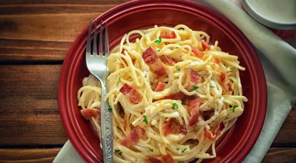 Pyszne spaghetti carbonara z chrupiącym boczkiem, posypane natką pietruszki. Idealne danie, gdy zastanawiasz się nad spaghetti carbonara kcal.