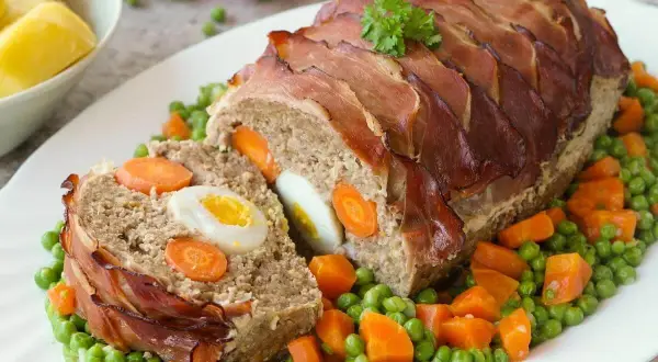 Fertiger Braten mit Speckmantel, gefüllt mit Ei und Karotten. Die Zubereitung Hase ist ein Genuss, serviert mit Erbsen und Karotten.