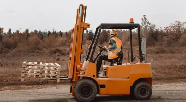 Operator wózka widłowego w kamizelce odblaskowej przewozi palety. Zarobki operatora wózka widłowego zależą od doświadczenia i miejsca pracy.