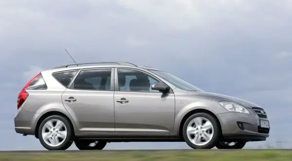 Srebrny Kia Ceed 1.6 benzyna w wersji kombi jedzie po drodze, za nim rozmyte zielone pola.