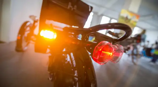 Blinker am Fahrrad leuchten orange und rot. Das Rücklicht ist klar erkennbar, während das vordere Licht diffus strahlt.