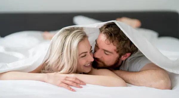 Ett par under täcket, hon ler, han viskar. Kanske en stund av ångest efter sex, eller bara intimitet.