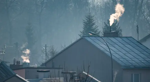 Dym z komina nad domami, czy spaliny z pieca gazowego są szkodliwe? Mglisty poranek nad miastem.