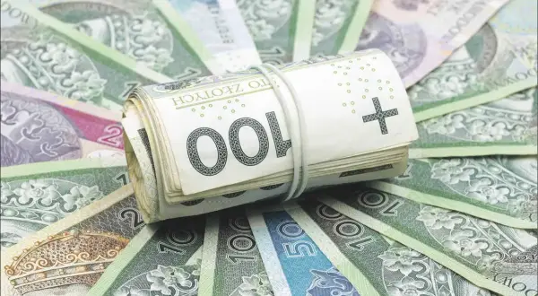 Zwijana rolka polskich banknotów 100 zł na tle innych banknotów.