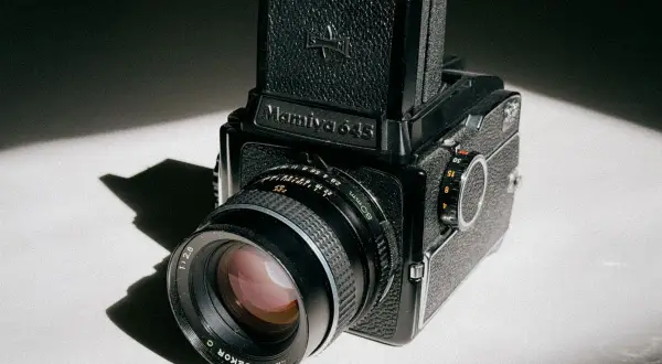 A classic Mamiya 645 medium format camera sits on a white surface, bathed in dramatic light and shadow.