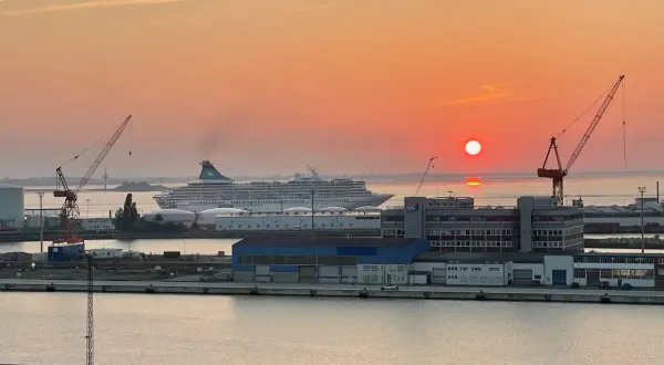Sonnenuntergang im Hafen. Ein großes Kreuzfahrtschiff liegt vor Anker, während Kräne und Gebäude der port agency im warmen Licht erstrahlen.
