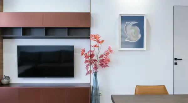 En modern inredning med en stor TV och flera tavlor runt om. En vas med röda höstblad står bredvid.