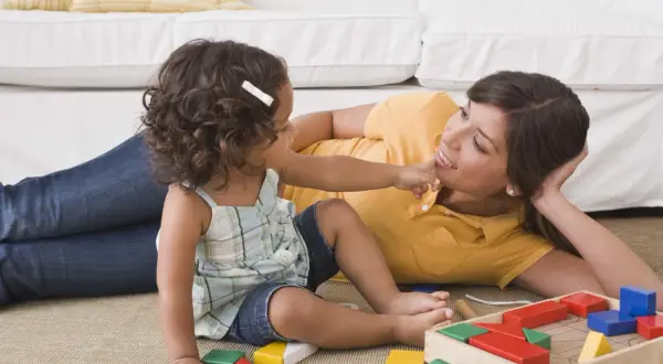 Mama uczy córkę, jak wychować dziecko, bawiąc się klockami na dywanie.