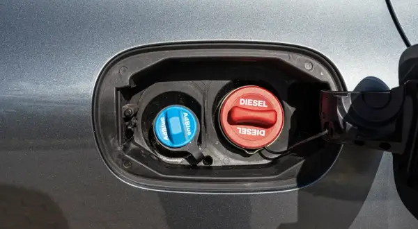Dwa korki wlewu paliwa w samochodzie: niebieski z napisem AdBlue i czerwony z napisem Diesel.