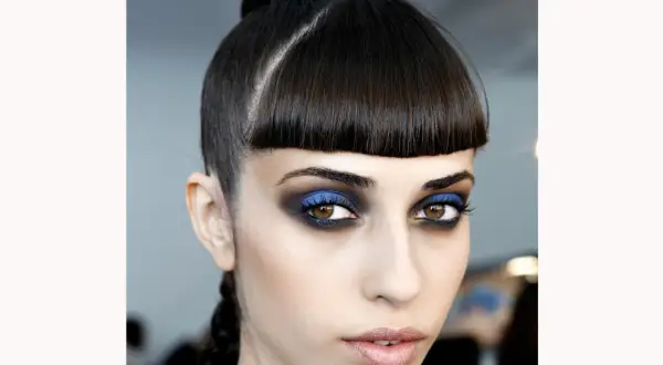 Occhi intensi con smokey eyes blu elettrico e nero, capelli raccolti in uno chignon e treccia.