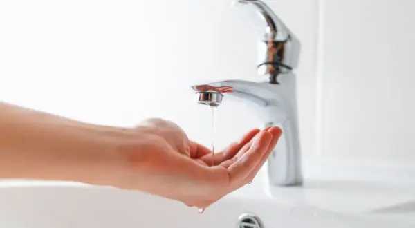 Main tenant, comment réduire la pression d'eau sur un robinet. Une main attrape un mince filet d'eau sortant d'un robinet moderne.