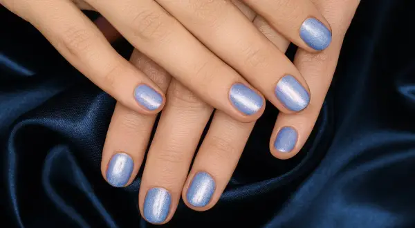 Mani curate con unghie corte rotonde smaltate di un azzurro perlato, adagiate su un tessuto blu notte.
