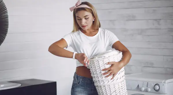Kobieta z koszem prania sprawdza godzinę, zastanawiając się, w ilu stopniach prać bieliznę.
