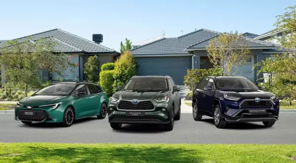Trzy modele toyoty crossover: zielona Corolla Touring Sports, ciemnozielony Highlander Hybrid i granatowy RAV4 Plug-in Hybrid, stoją przed domami.