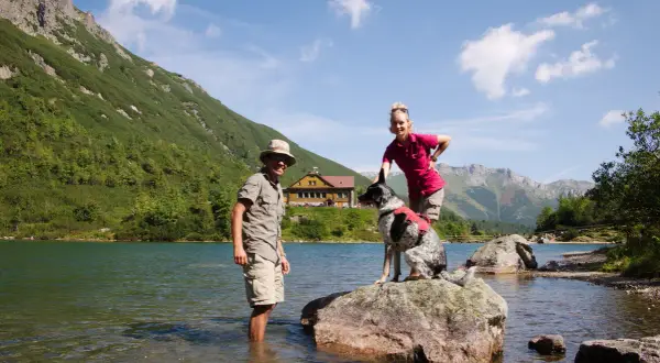 Para na tle górskiego jeziora i schroniska, ubrana w odzież Craghoppers, co to za firma? Piesek na skale.