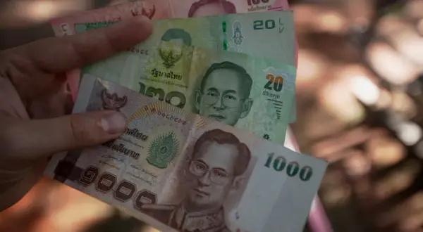 Ręka trzyma tajskie banknoty: 1000, 100, 20 bahtów. Planujesz podróż i zastanawiasz się, jakie dolary do Tajlandii zabrać? Lepiej wymienić na bahty.