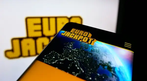 Logo Eurojackpot na ekranie telefonu z widokiem Europy nocą.
