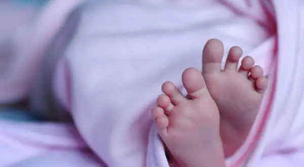 Małe stópki noworodka w różowym otulaczu. Warto wiedzieć, gdzie złożyć wniosek o becikowe, by otrzymać wsparcie na start.