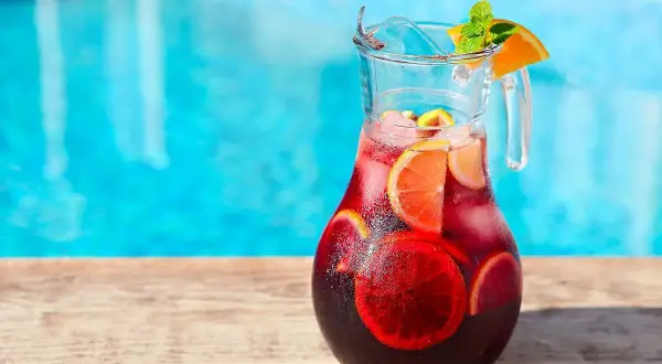 Pichet de sangria recette, rempli de fruits et de glaçons, prêt à être dégusté au bord de la piscine.