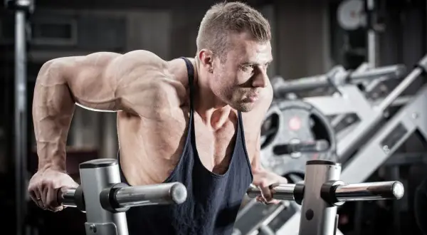 Mięśniowy mężczyzna wykonuje pompki na poręczach, jedno z najlepszych ćwiczeń na triceps.
