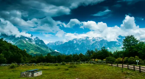 Majestuoso mirador de los Picos de Europa con nubes dramáticas sobre picos nevados y un prado verde.