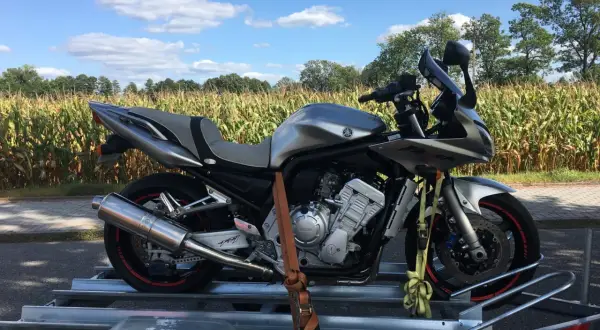 Srebrny motocykl Yamaha Fazer na przyczepce, gotowy do przerejestrowania. W tle pole kukurydzy i błękitne niebo.