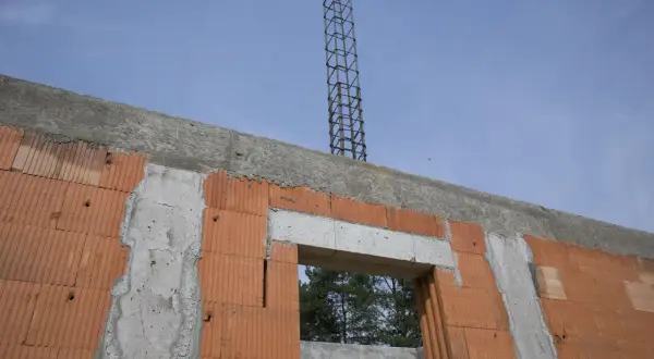 Budowa domu, widoczny fragment ściany z pustaków ceramicznych, betonowy nadproże okna i zbrojenie słupa. Wieniec opuszczony, czekający na dalsze prace.