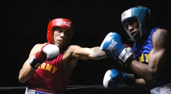Two boxers, one in red with "ARMY" on his vest, the other in blue, engage in intense **sparring**. Their gloves are raised, ready for the next move in this practice bout.