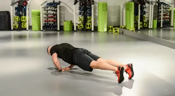 Mężczyzna wykonuje pompki diamentowe na siłowni, ćwicząc klatkę piersiową i triceps.
